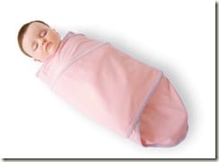 A sleeping baby wrapped snugly in a pink swaddle blanket, lying on a white surface.