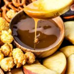 A close-up of an autumn snack board recipe showcases a spoon drizzling caramel over a wooden bowl. Surrounding it are apple slices, popcorn, and pretzels. Text overlays highlight AUTUMN board and EASY recipe.