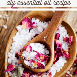A wooden heart-shaped bowl brimming with coarse sea salt and dried rose petals, crowned by a wooden spoon holding the same blend. Text reads, Rose Bath Soak Recipe: DIY Essential Oil Delight.