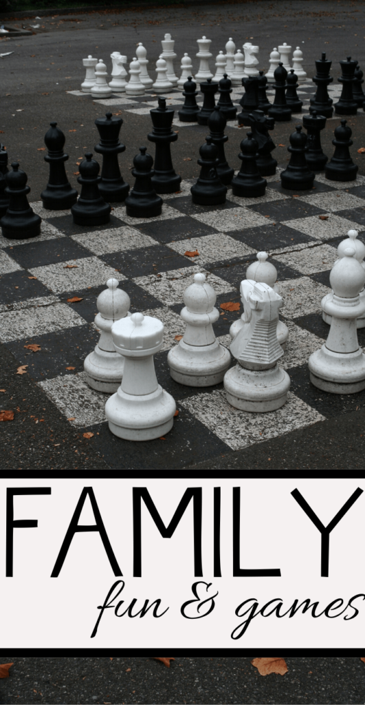 Giant chess set on an outdoor board with large black and white pieces. The image has the text Family fun & games at the bottom. Fallen leaves are scattered on the ground.