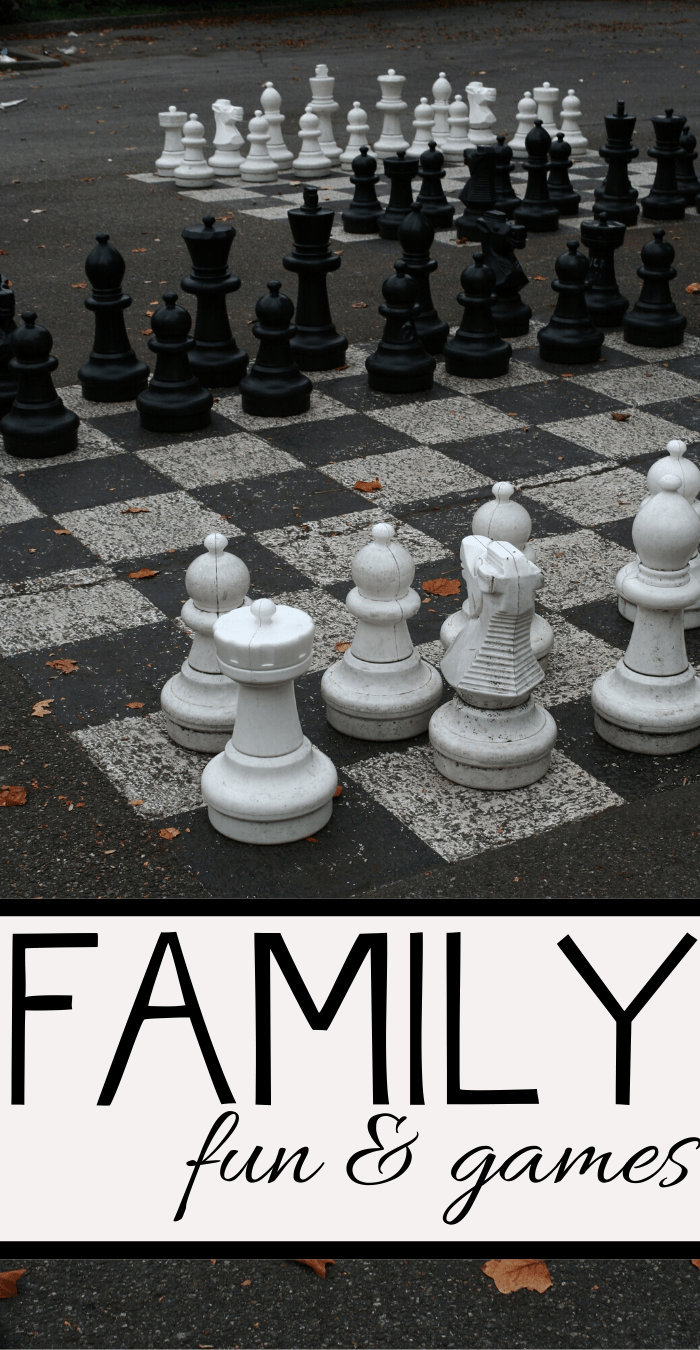 Giant chess set on an outdoor board with large black and white pieces. The image has the text Family fun & games at the bottom. Fallen leaves are scattered on the ground.