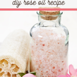 A glass jar filled with pink bath salts is surrounded by pink rose petals, a loofah, and a towel. Text above reads, Essential Oil Bath Soak: DIY Rose Bath Soak Recipe.