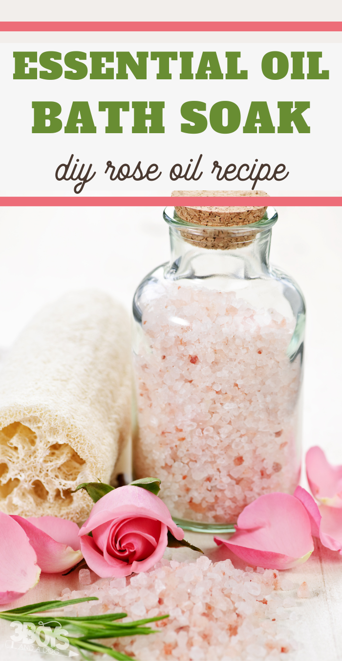 A glass jar filled with pink bath salts is surrounded by pink rose petals, a loofah, and a towel. Text above reads, Essential Oil Bath Soak: DIY Rose Bath Soak Recipe.